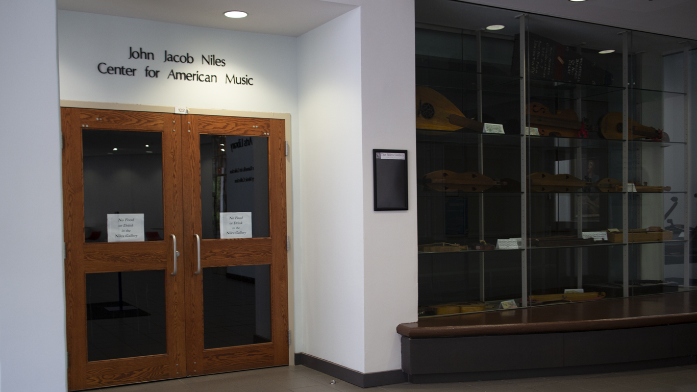 Glass double doors serve as an entrance to the Niles Galery. A glass case to the right displays several historic dulcimers and other folk instruments.