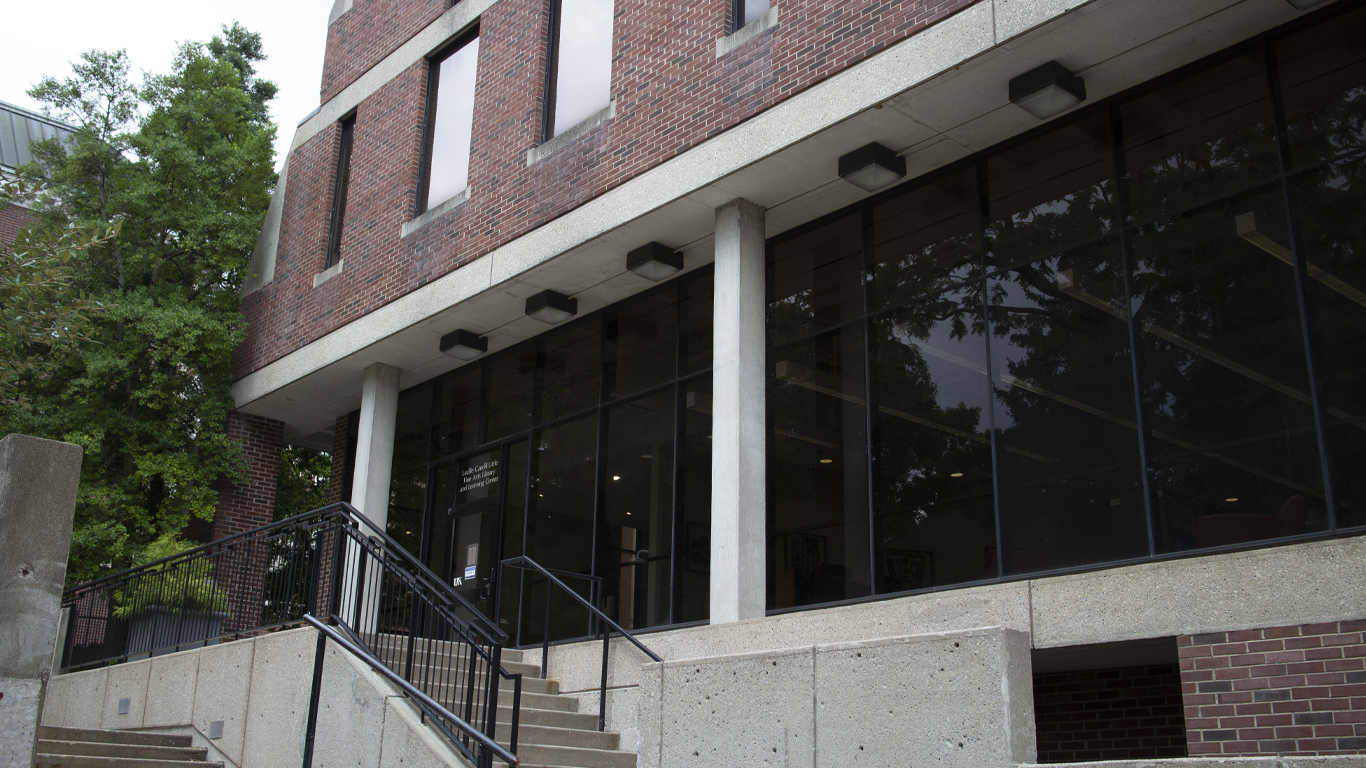 The Patterson drive entrance of the Fine Arts Library. Stairs lead up to a doorway in a glass wall. A ramp is nearby to wrap around to the front entrance of the library.