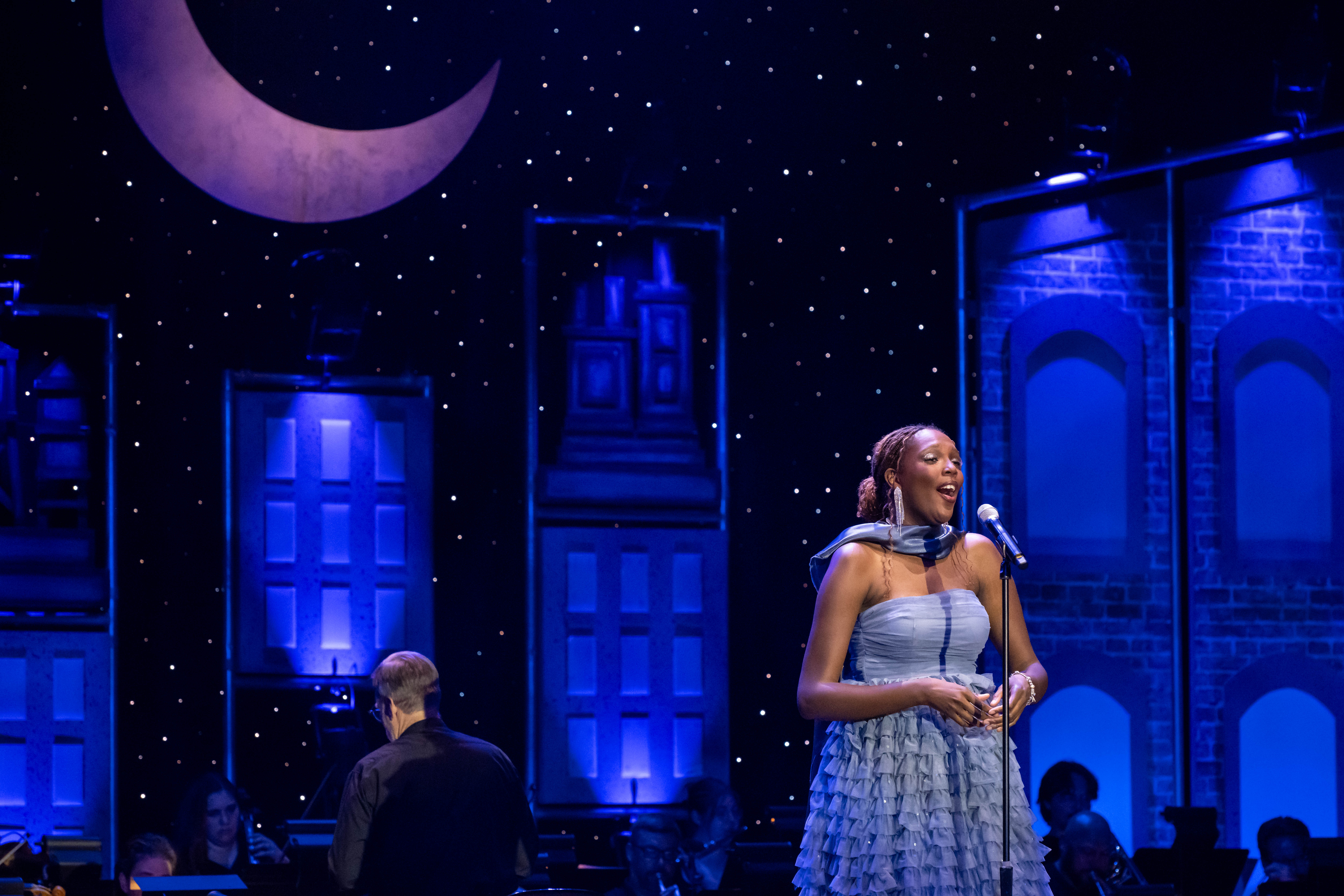 person in blue dress singing on stage, musician in background