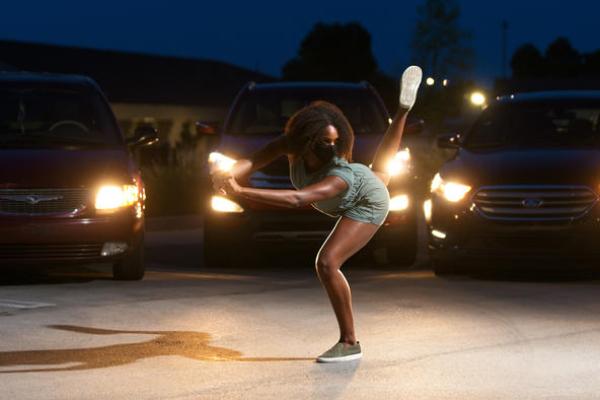 dancer in mask in parking lot surrounded by cars