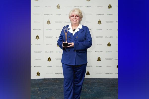 Image of Renee Cobb wearing a blue suit in front of a step and repeat holding her award