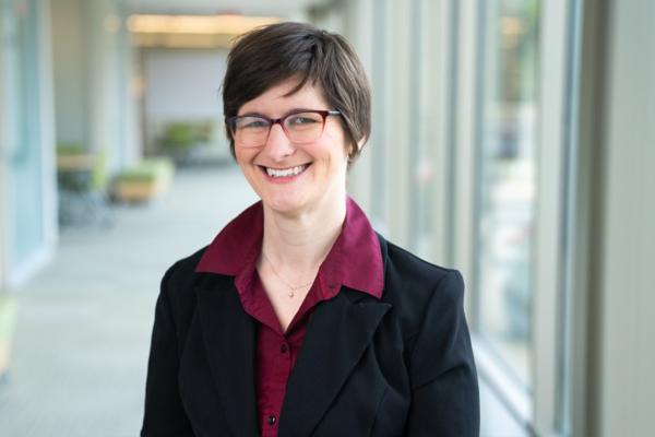Abigail Van Klompenberg in a black blazer and red shirt, wearing glasses.