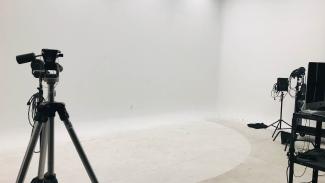 A blank white room with several tripods, stands, lighting kits, a computer cart, and wiring ready to go for a photoshoot.
