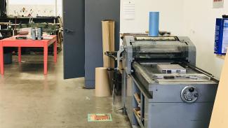 A large gray letterpress machine takes up one wall, with nearby cabinet and red worktable.