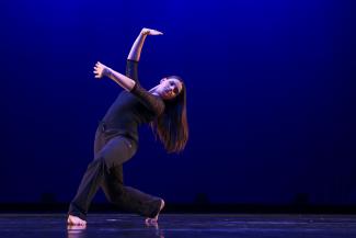 Dancer in lunge on stage with arms lifted