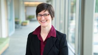 Abigail Van Klompenberg in a black blazer and red shirt, wearing glasses.