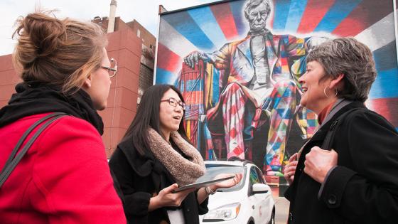 three people talking in front of outdoor mural