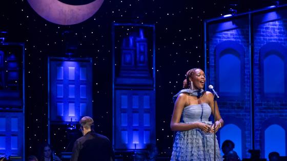 person in blue dress singing on stage, musician in background
