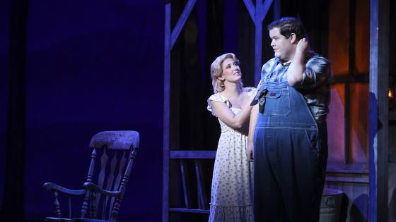 two singers on stage in front of shed and rocking chair
