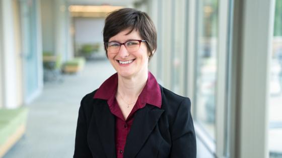 Abigail Van Klompenberg in a black blazer and red shirt, wearing glasses.