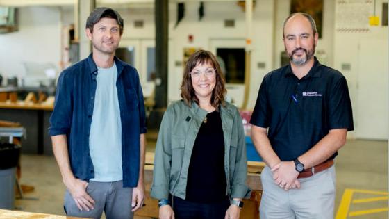 three people looking at the camera in a wood shop