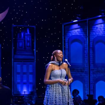 person in blue dress singing on stage, musician in background